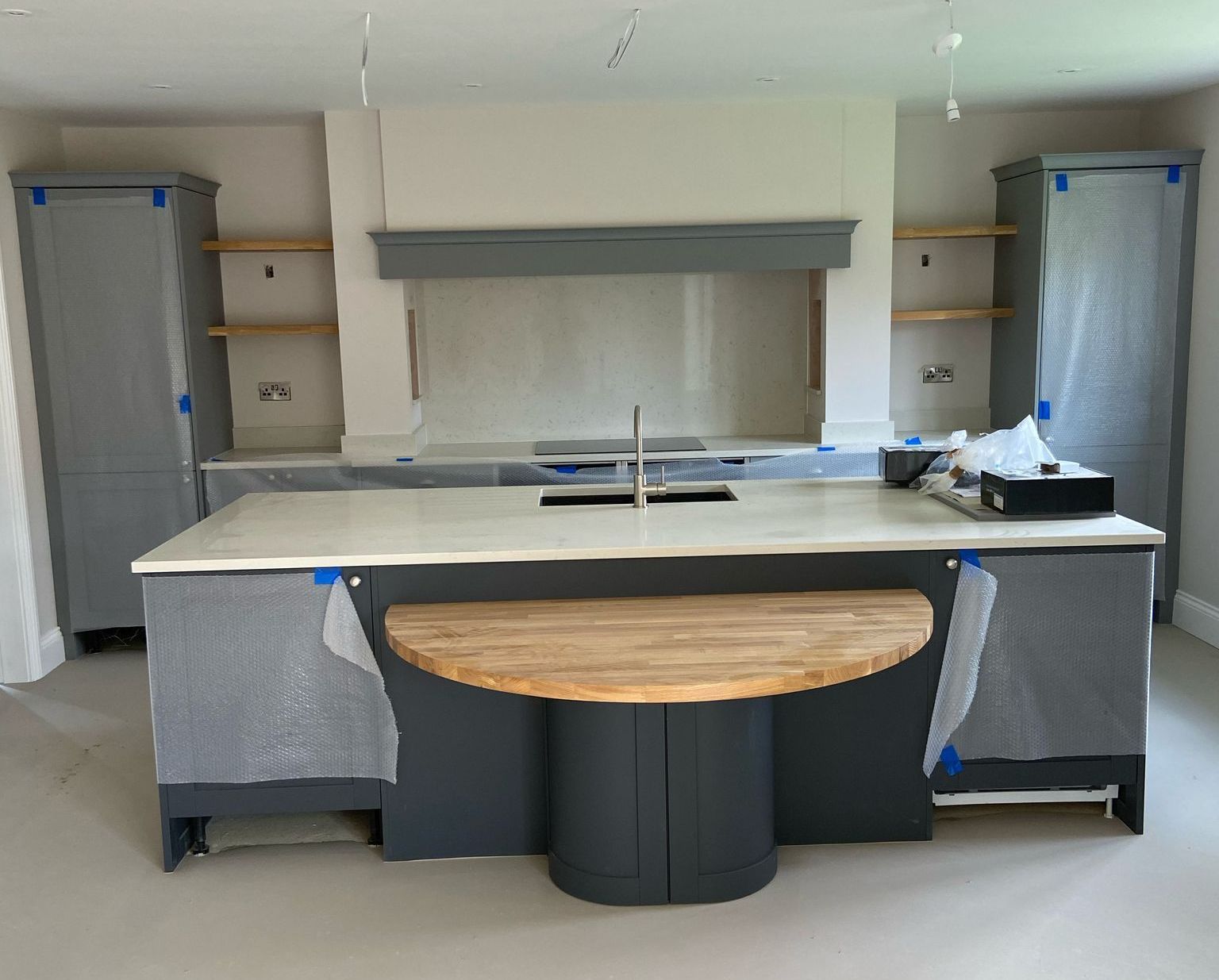 Gray kitchen with island and light wood breakfast bar. Cabinets are covered in protective wrap.