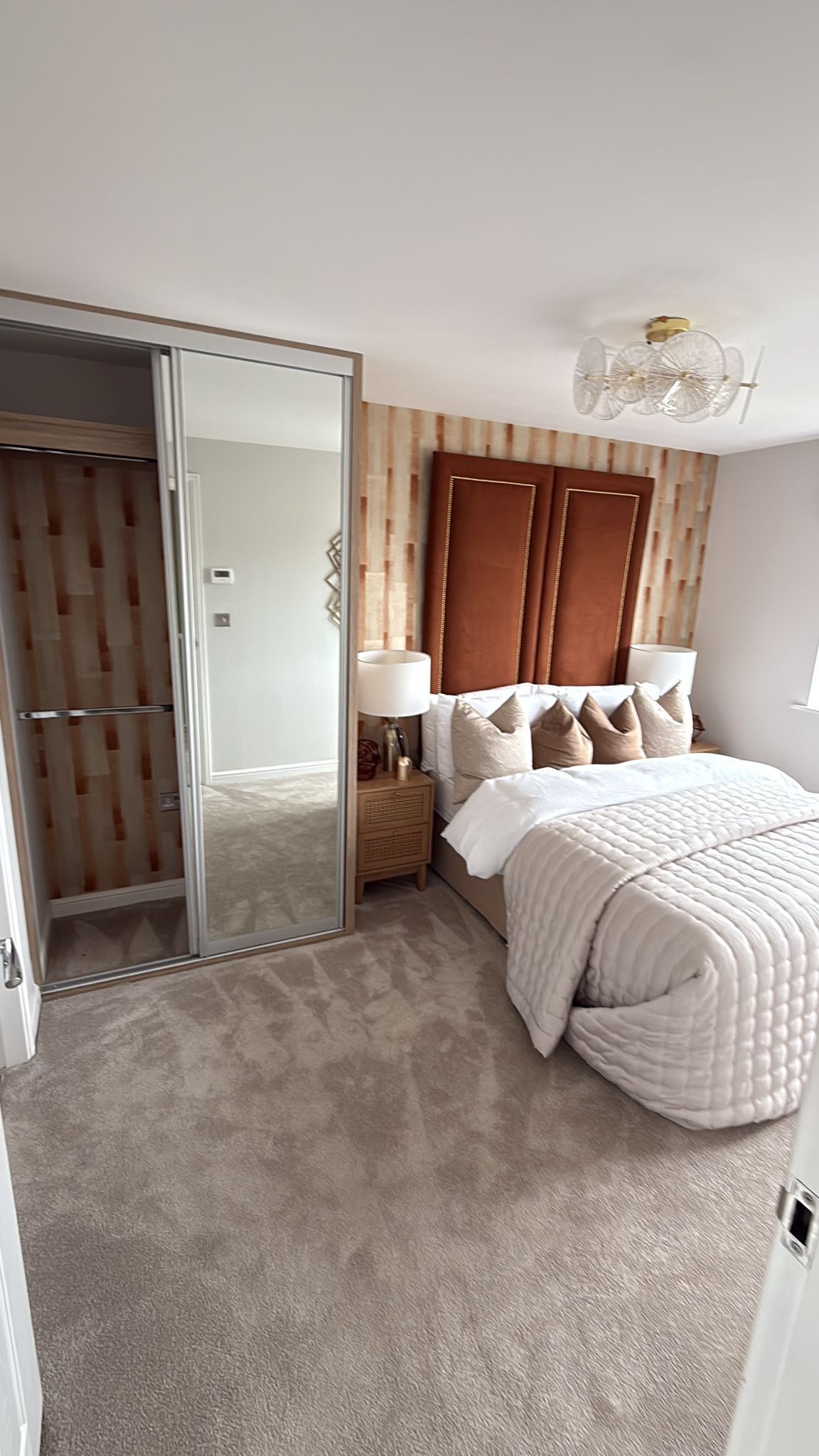 Bedroom with large mirrored closet, light-colored carpet, bed with beige bedding, and wood paneling on the wall.