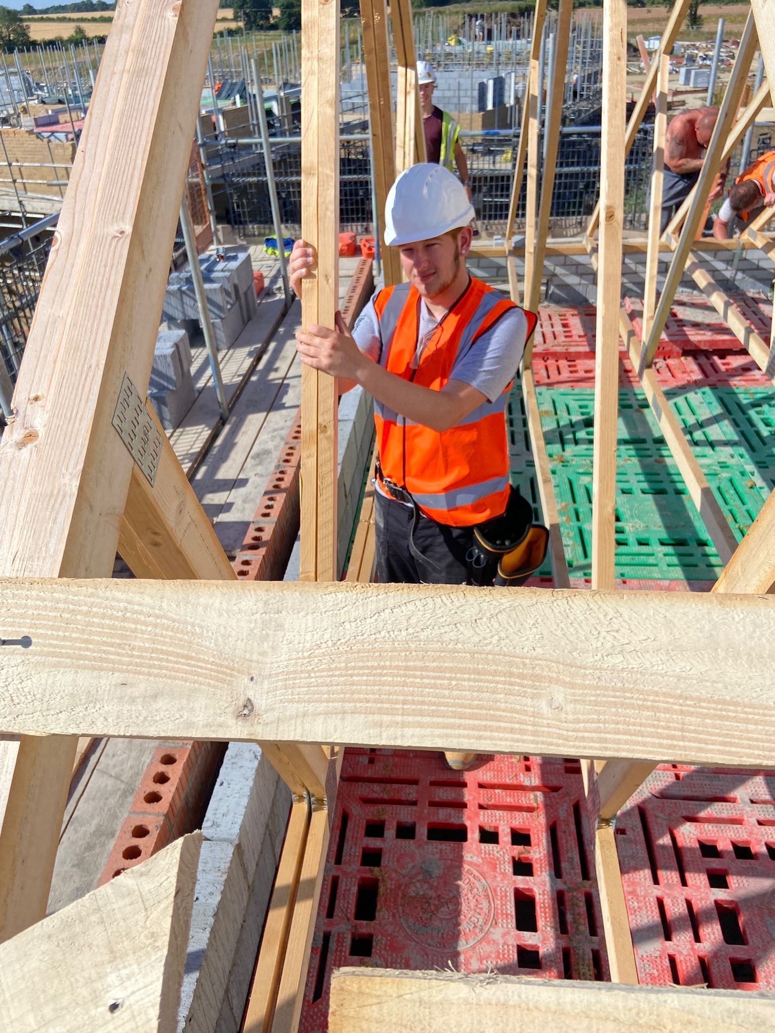 Construction worker, wearing a hard hat and orange vest, installing a wooden beam on a roof.