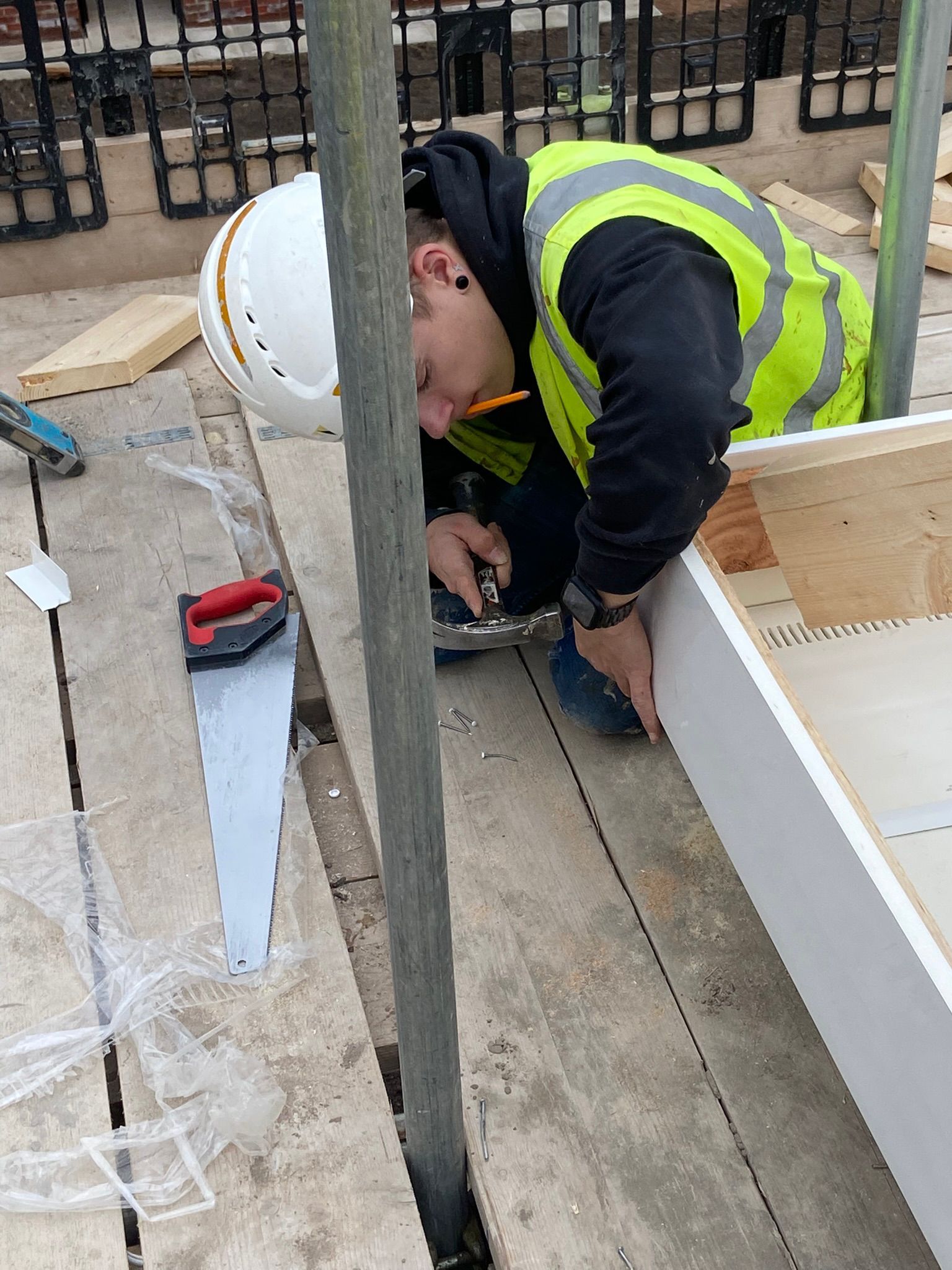 Construction worker wearing safety gear using a saw on a wooden structure.