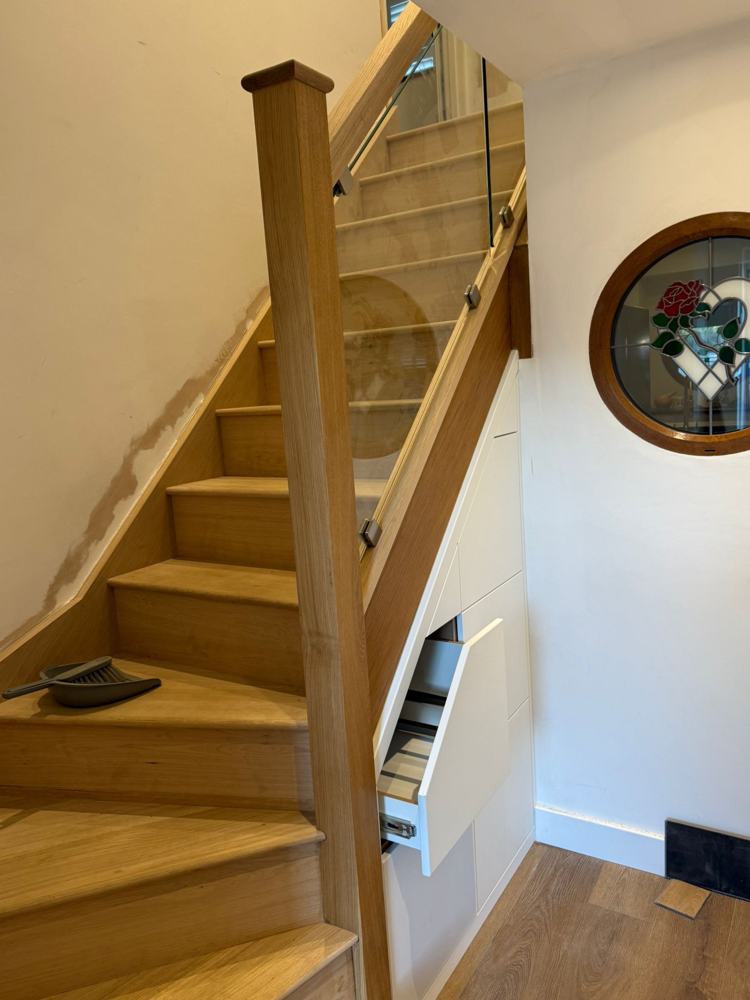 Wooden staircase with glass railing, built-in storage, and a round stained-glass window.
