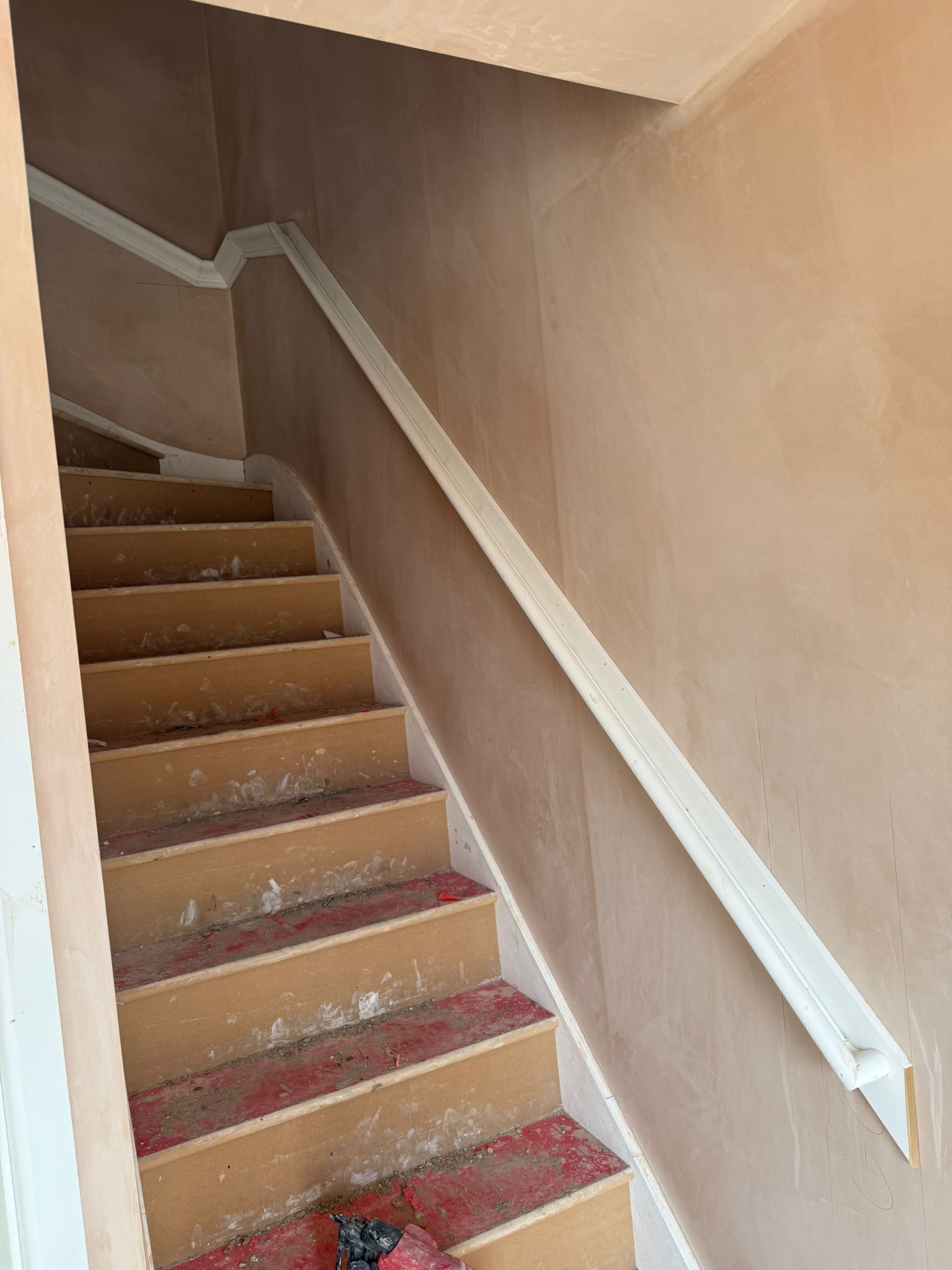 Staircase with a newly installed white handrail. The walls and steps are unfinished and have a pinkish hue.
