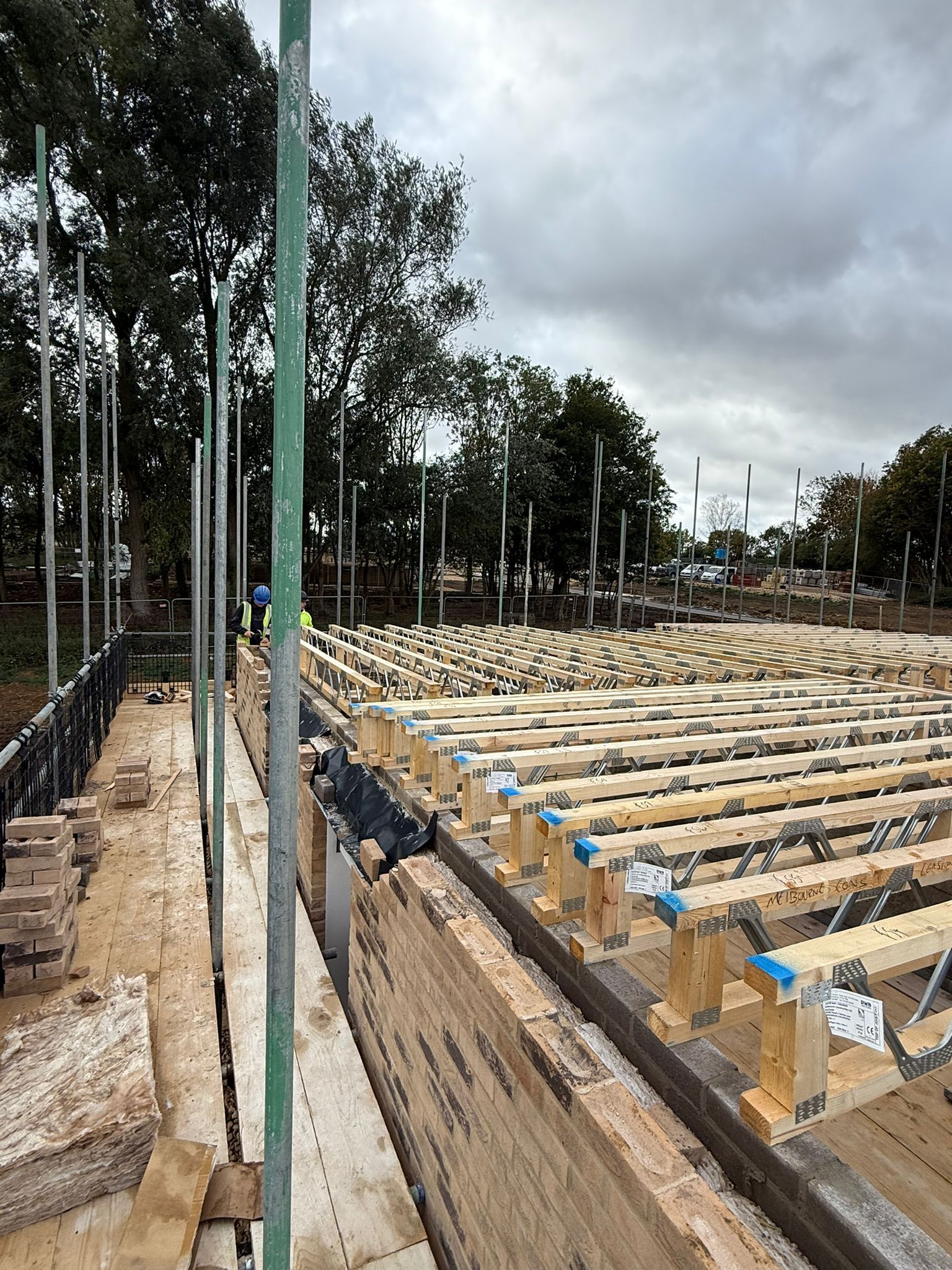 Construction site with exposed wooden beams, brickwork, and scaffolding under a cloudy sky.