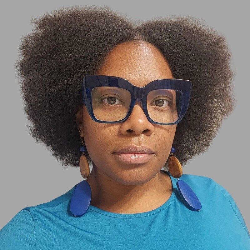 A woman wearing glasses and earrings is wearing a blue shirt.
