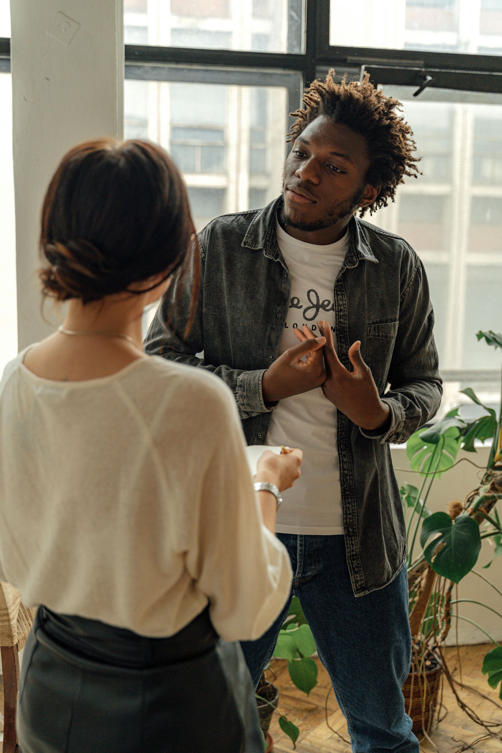 A man and a woman are talking to each other in front of a window.