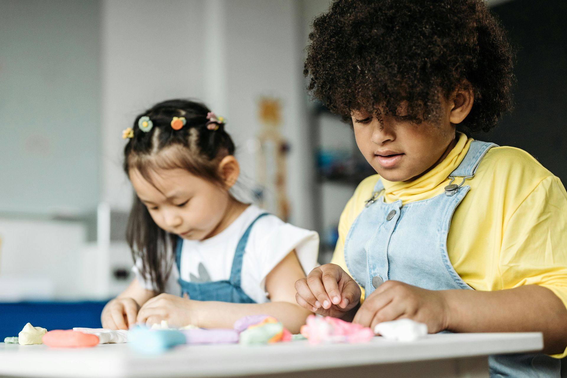 A boy and a girl are sitting at a table playing with play dough.