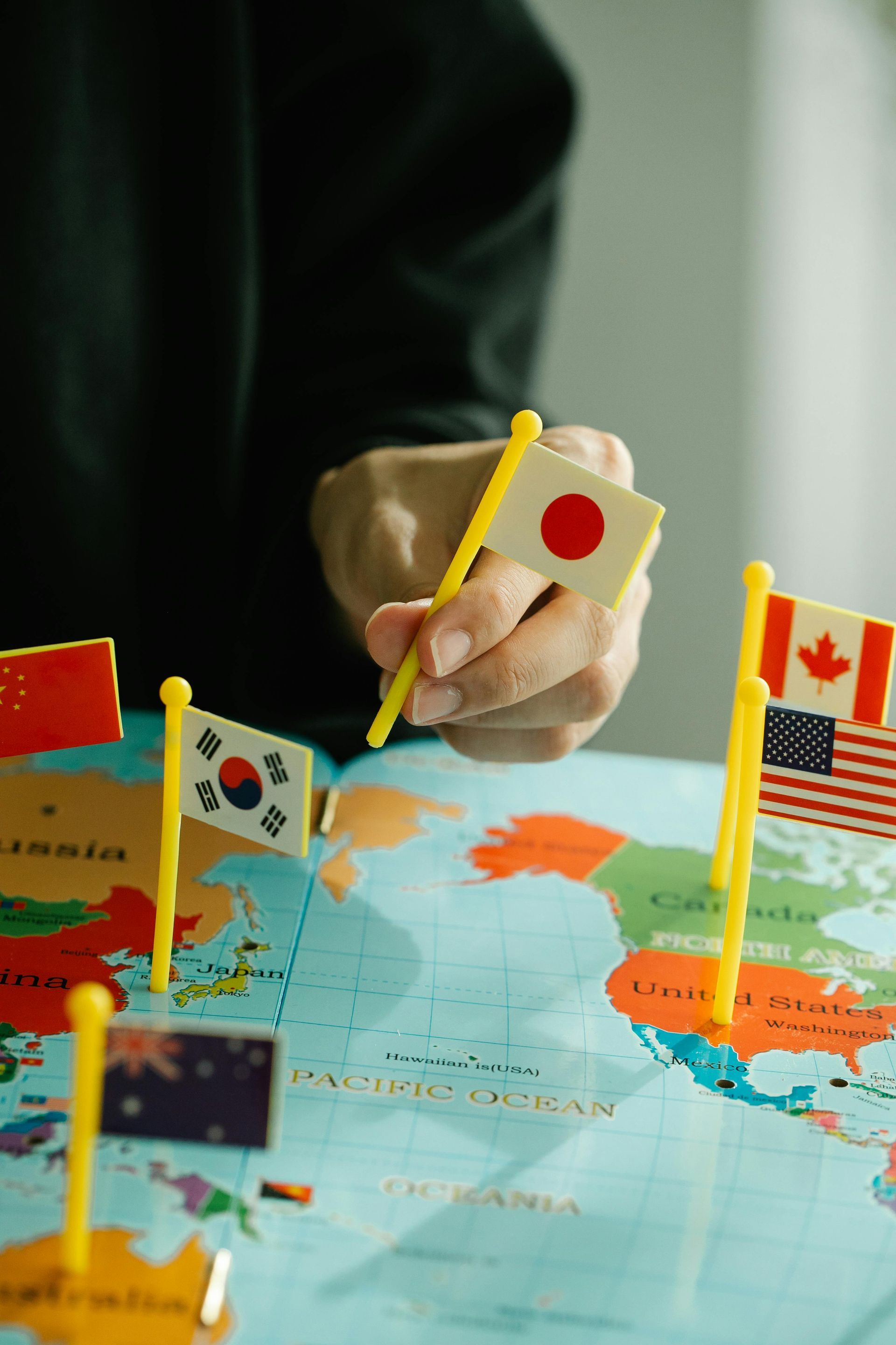 Hand placing a Japan flag on a world map with other international flags visible