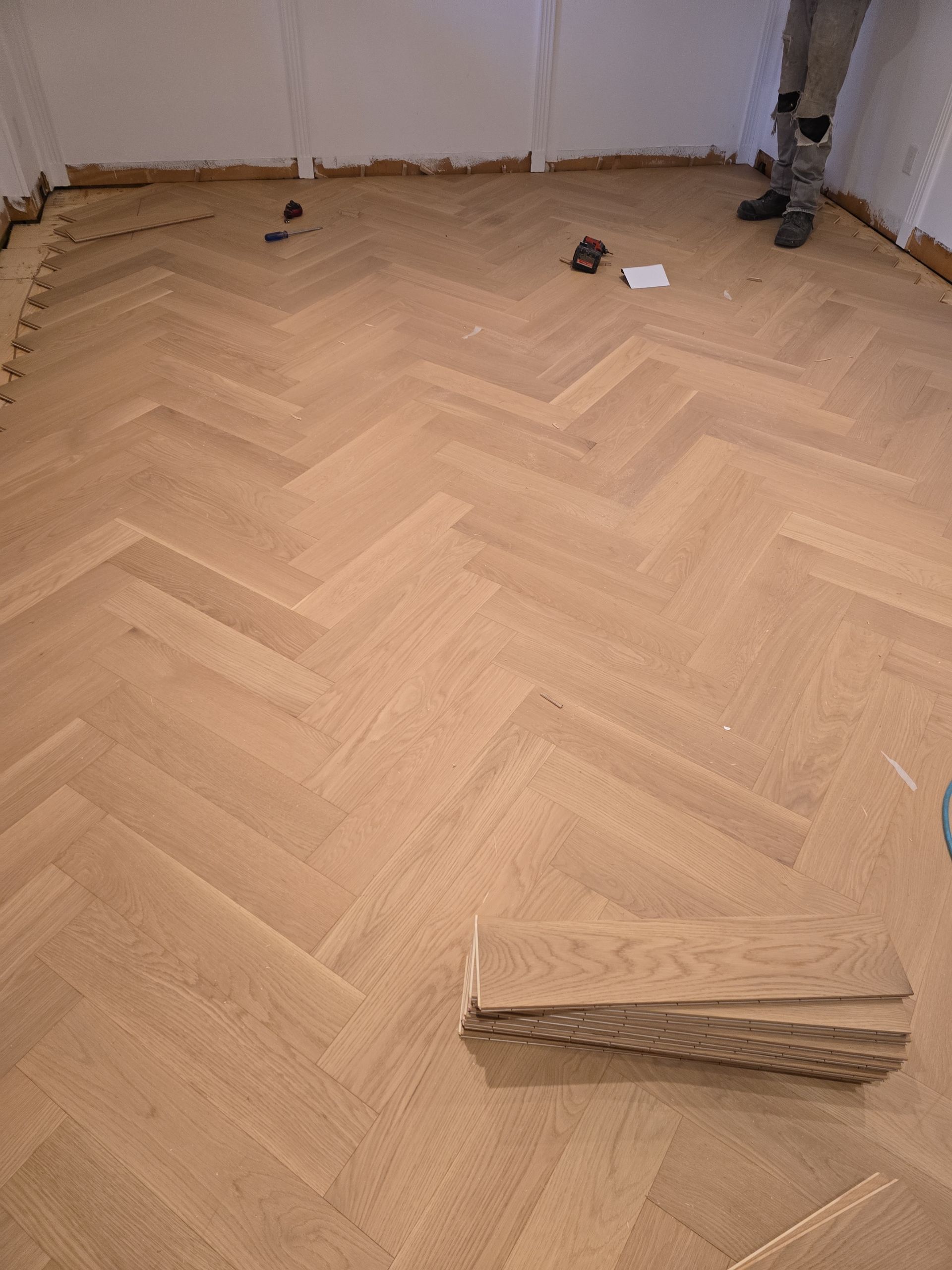 Une personne se tient debout sur un plancher en bois avec un motif à chevrons.
