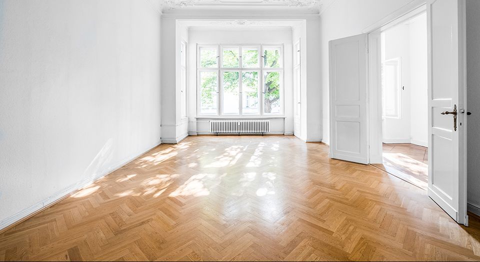 Un salon vide avec du parquet et des murs blancs.