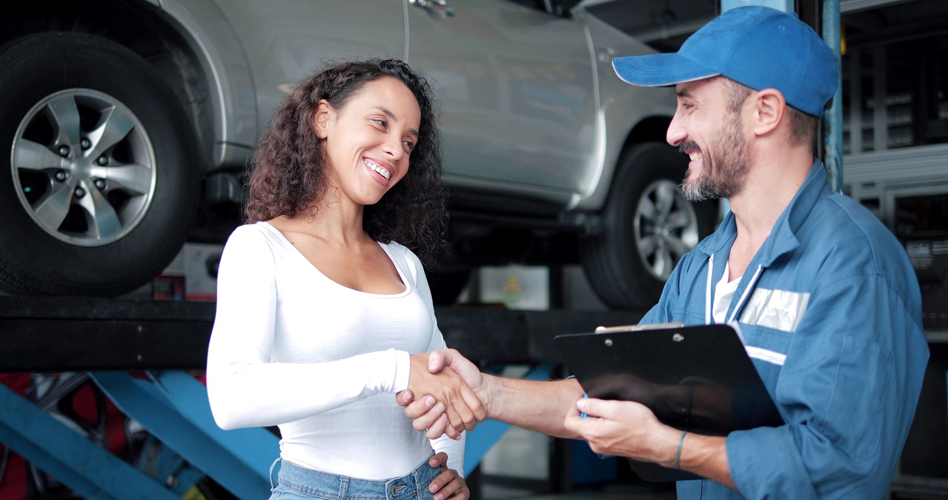 A woman is shaking hands with a mechanic in a garage.