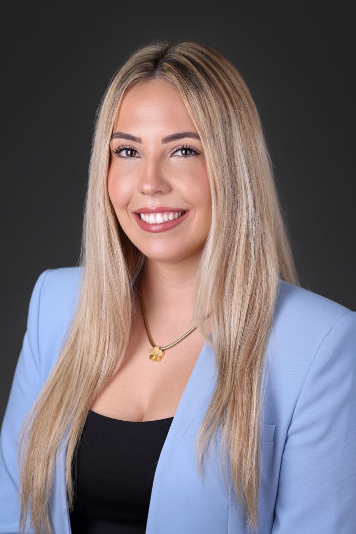 A woman with long blonde hair is wearing a blue jacket and smiling.