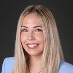 A woman with long blonde hair is smiling and wearing a blue jacket.