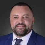 A man with a beard is wearing a blue suit and tie.