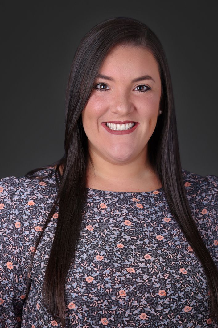 A woman with long hair is smiling and wearing a floral shirt.