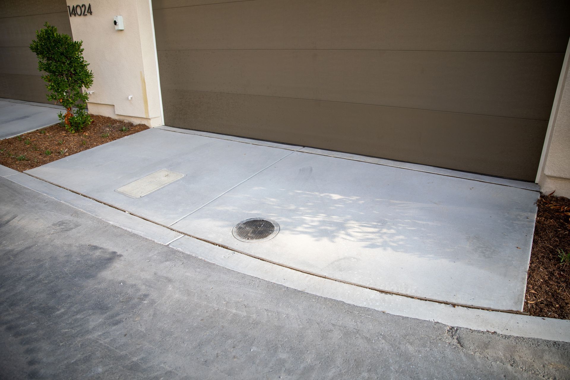 A concrete driveway next to a garage with a manhole cover.