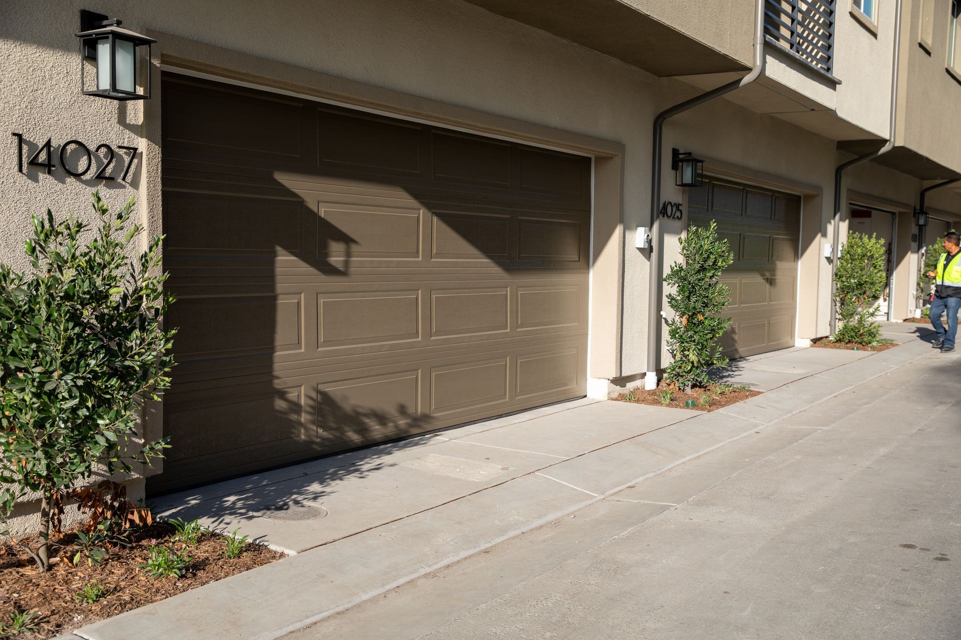 A man in a yellow vest is walking down a sidewalk in front of a building with garage doors.