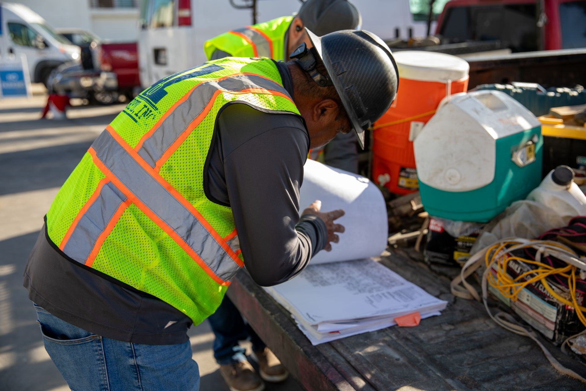 A man in a safety vest and hard hat is looking at a piece of paper.