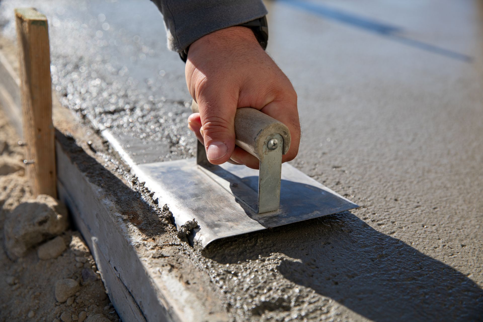 A person is using a trowel to spread concrete on a sidewalk.