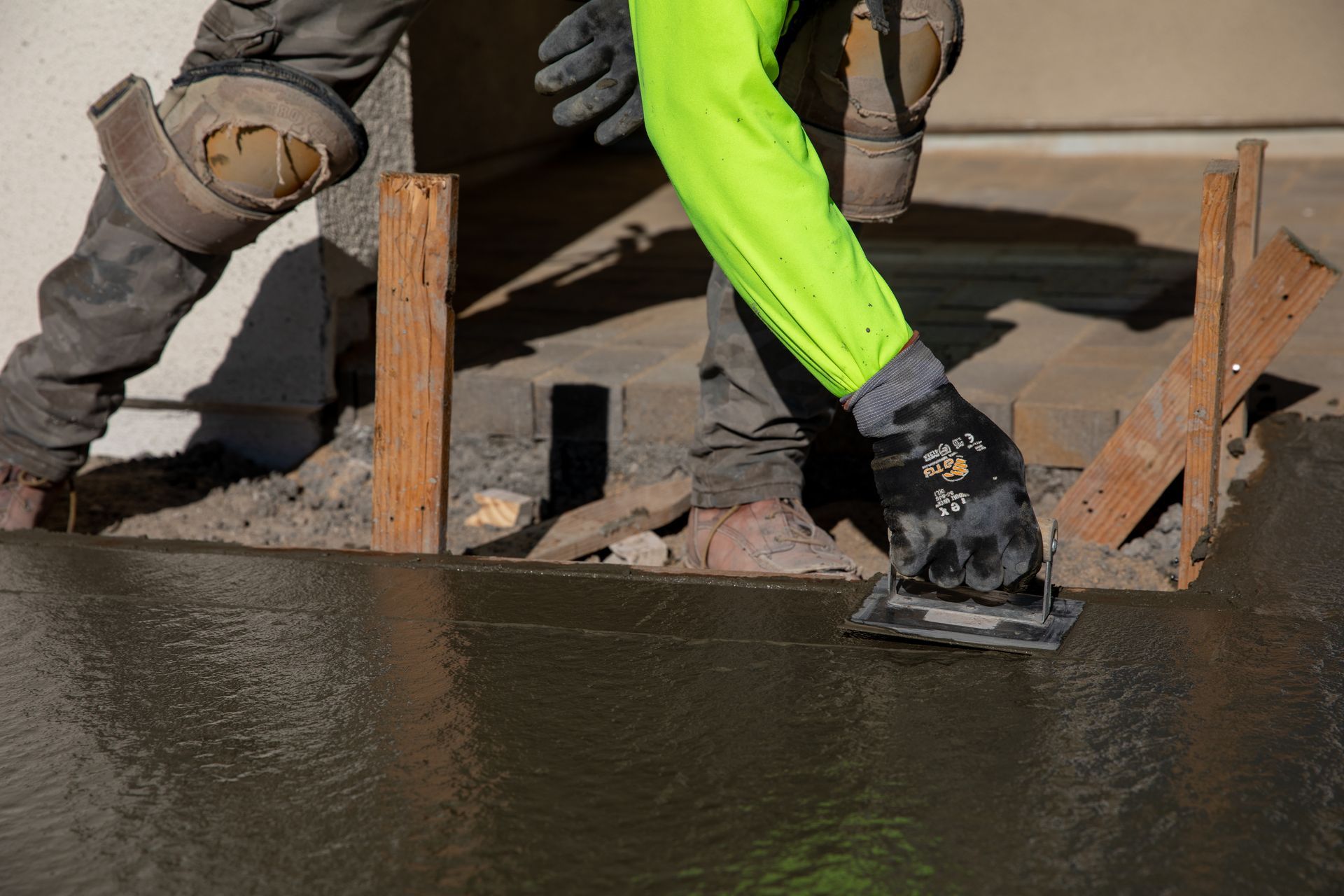 A construction worker is spreading concrete on a sidewalk.