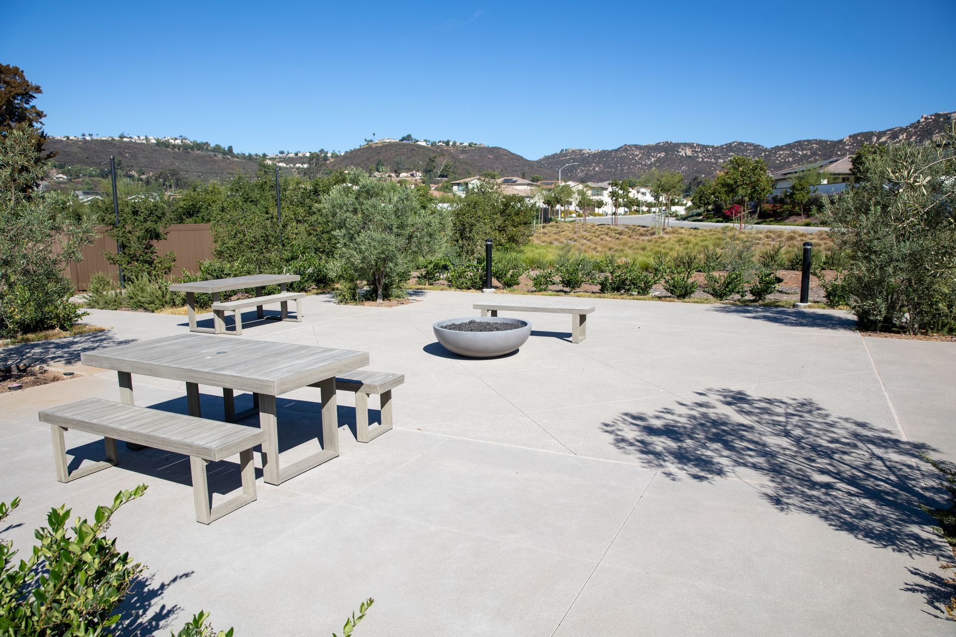 Park area with concrete picnic table and benches, fire pit, and trees, with hills in background.