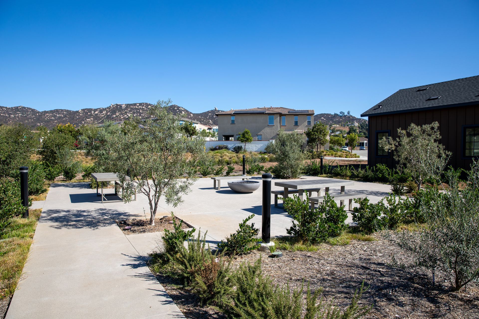 A concrete walkway leading to a picnic area with a house in the background.