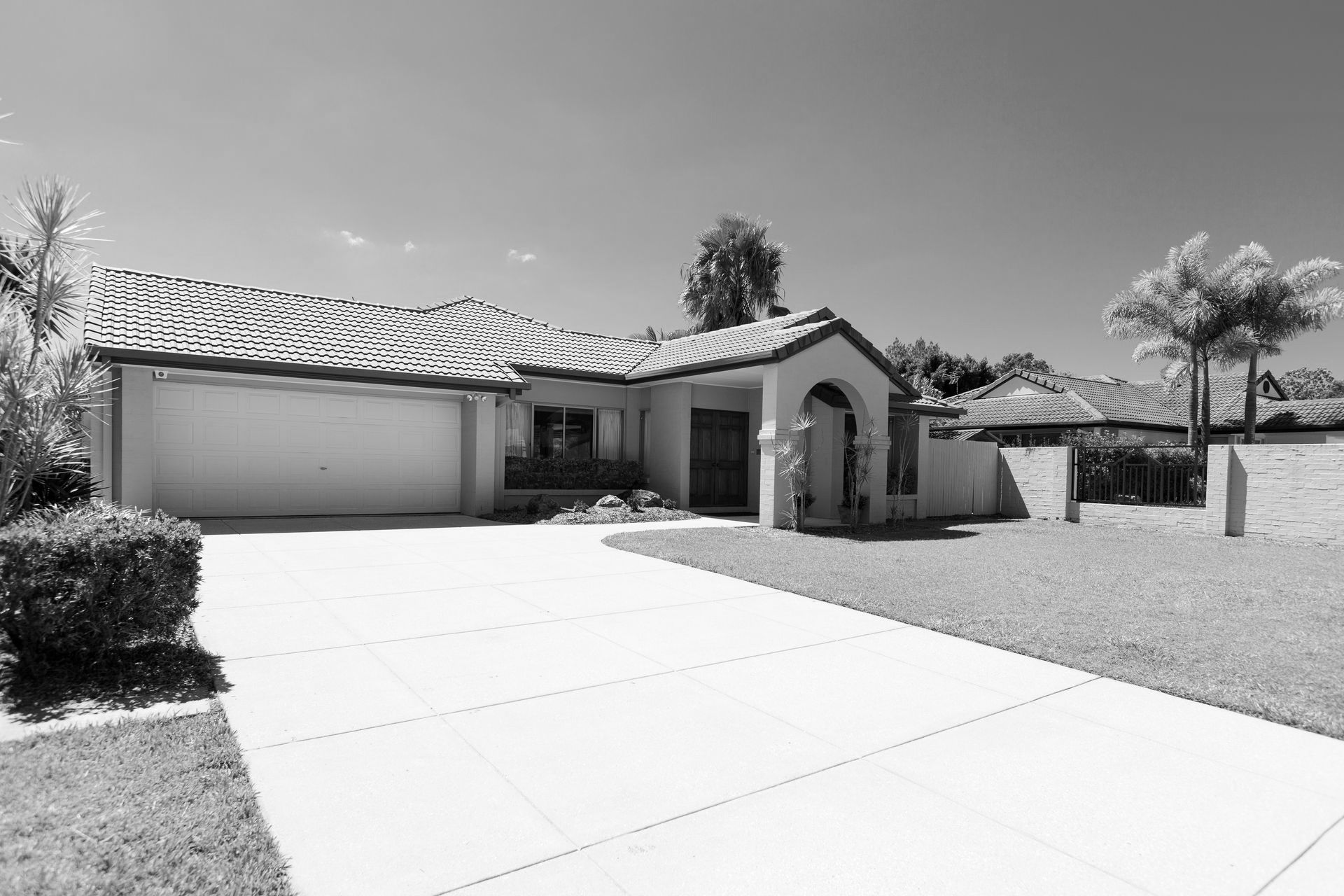 A black and white photo of a house with a driveway leading to it.