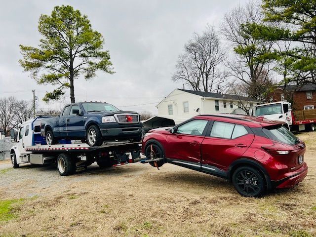 A tow truck is towing a red suv and a blue truck.
