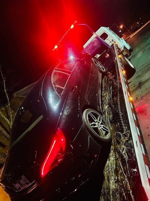 A car is being towed by a tow truck at night.