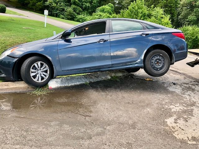 A blue car is stuck in a puddle on the side of the road.