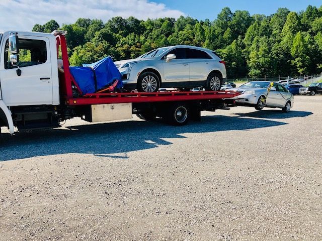 A tow truck with a car on the back is parked in a gravel lot.