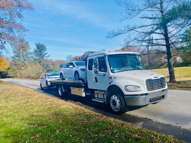 A tow truck is towing two cars down a road.