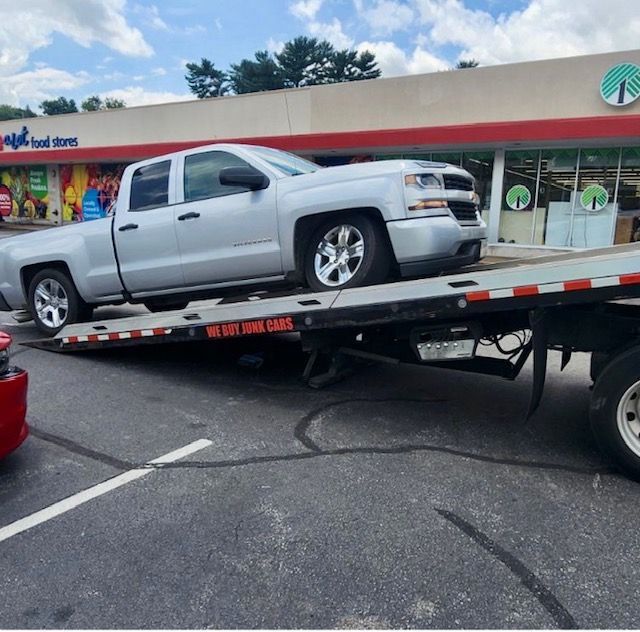 A silver truck is being towed by a flatbed tow truck