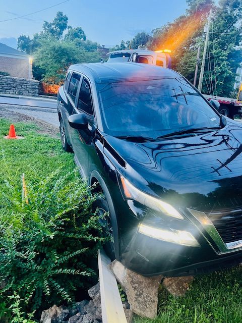 A black car is parked on the side of the road next to a bush.