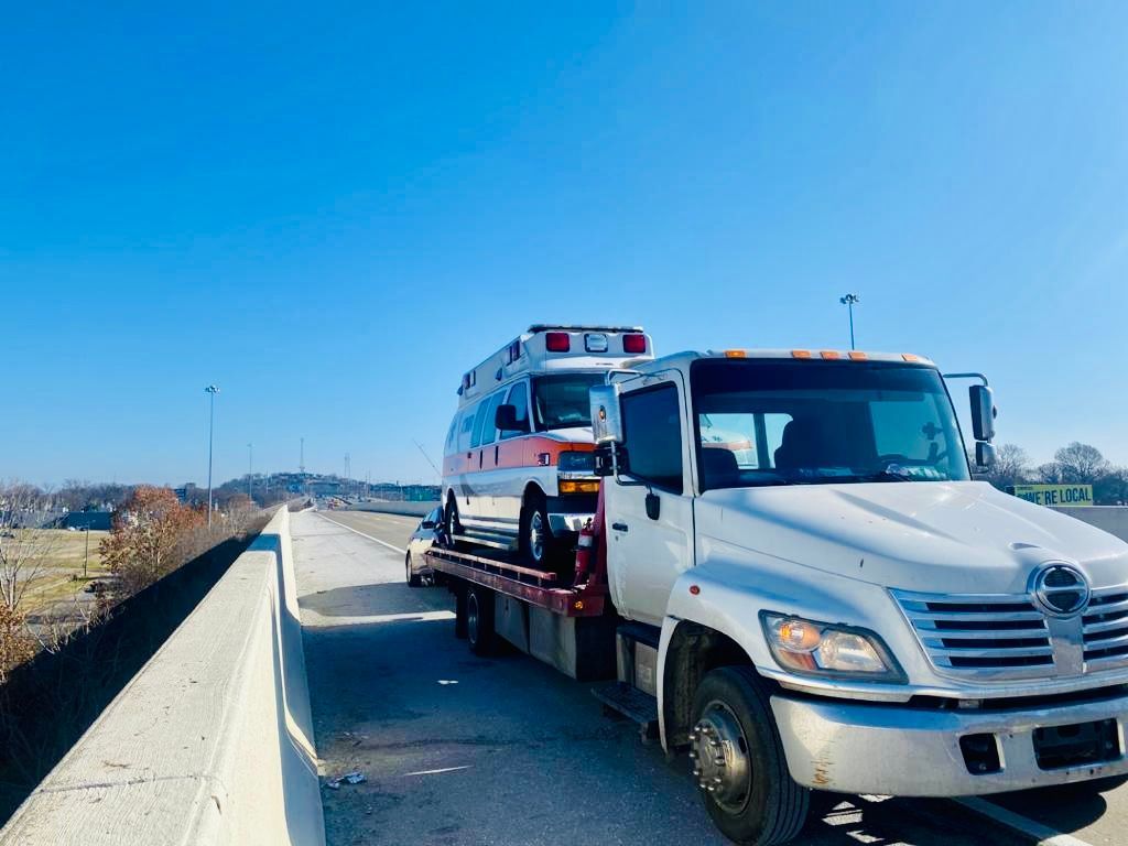 An ambulance is being towed by a tow truck on a highway.