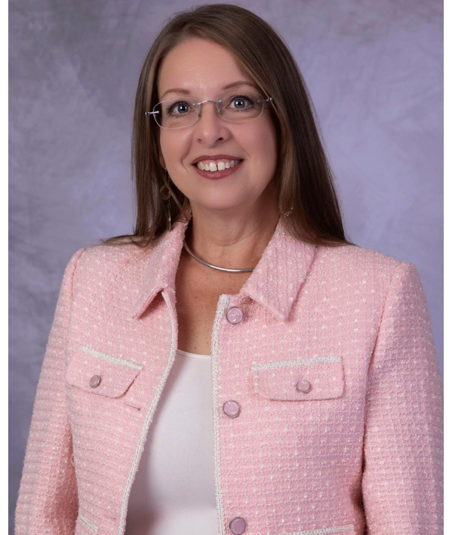 A woman wearing glasses and a jacket is smiling for the camera.