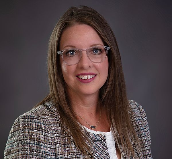 A woman wearing glasses and a jacket is smiling for the camera.