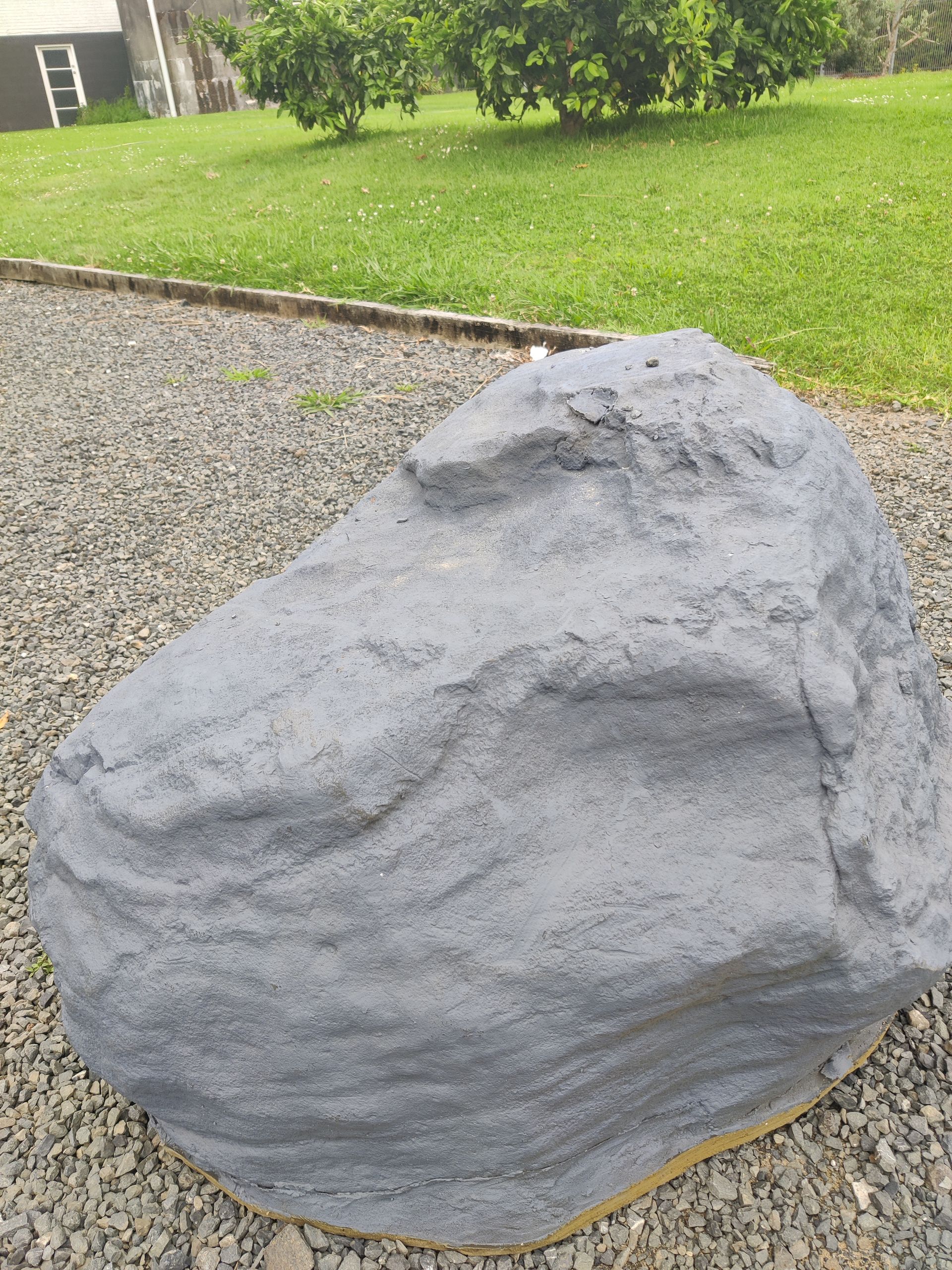 A large rock is sitting on top of a gravel driveway.