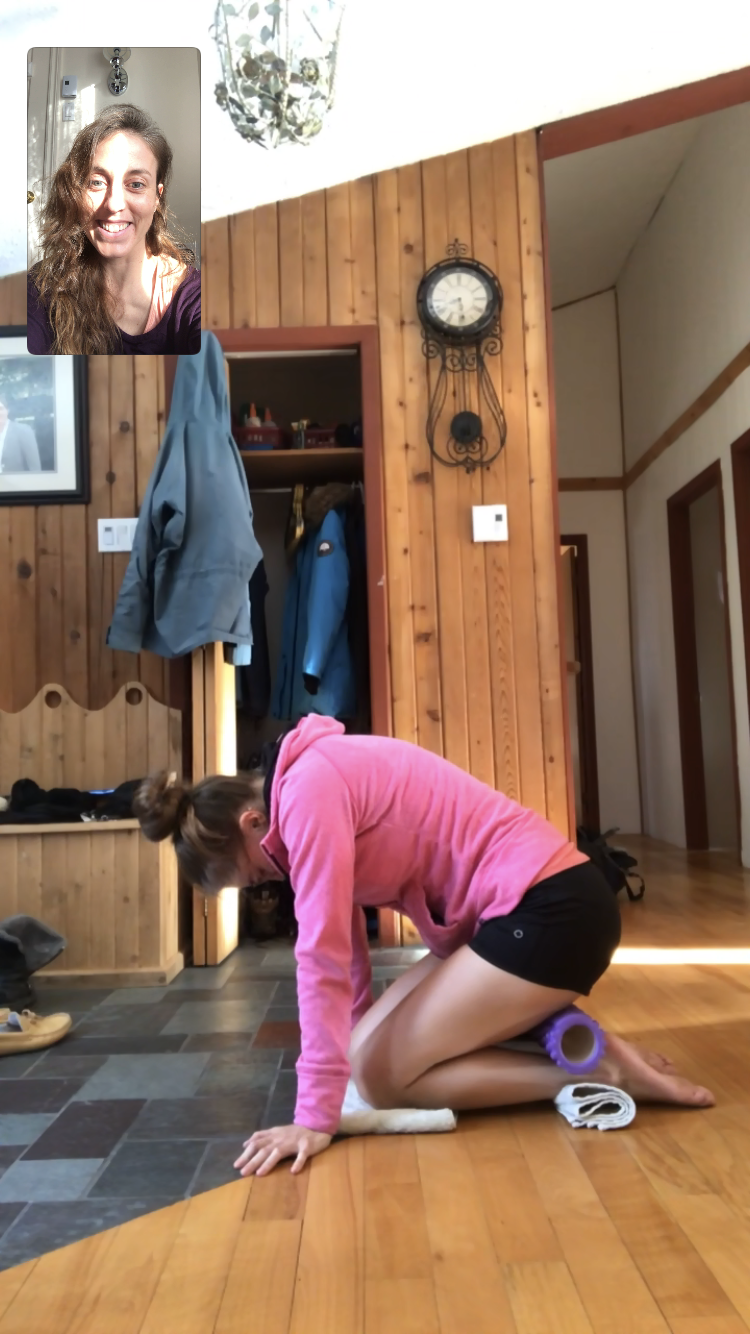 A woman in a pink shirt is kneeling on the floor while talking to another woman on a video call.