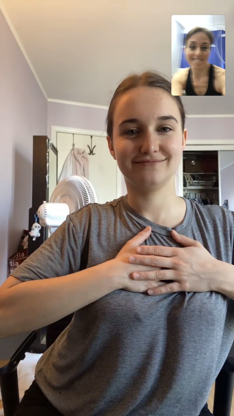 A woman is sitting in a chair with her hands on her chest while talking to another woman on a video call.