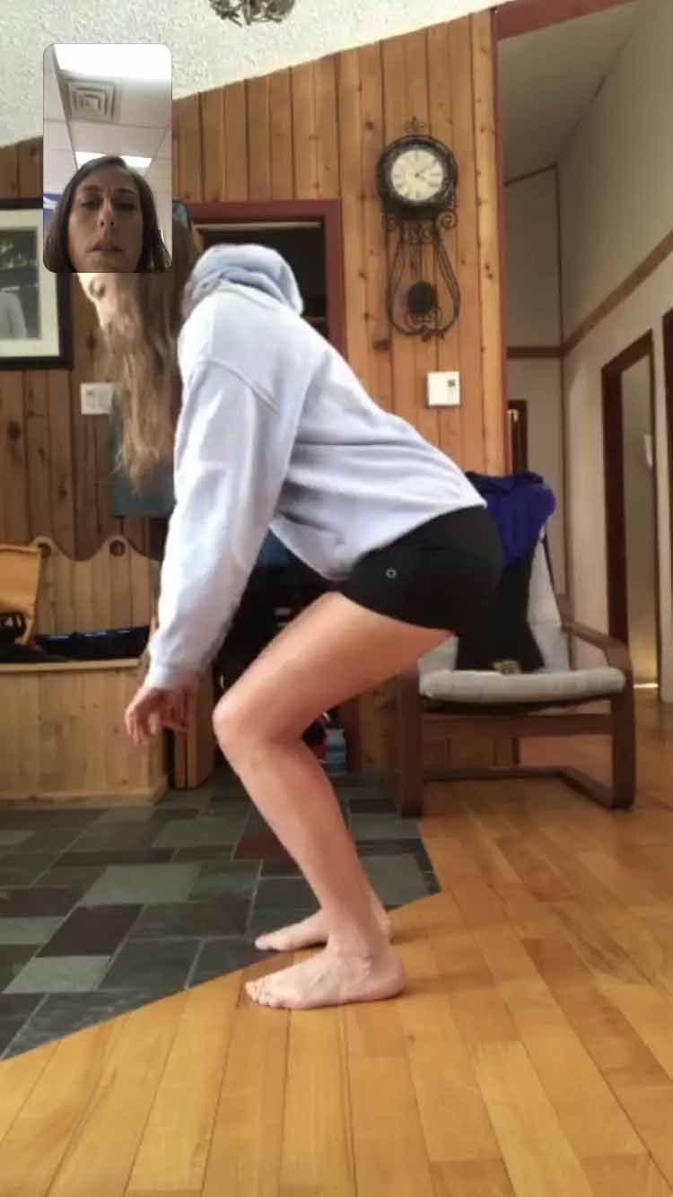 Une femme est accroupie sur un plancher en bois devant un miroir.