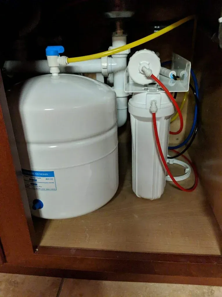 Under-sink reverse osmosis water filtration system with white tank and filters, various tubes, and a faucet connector.