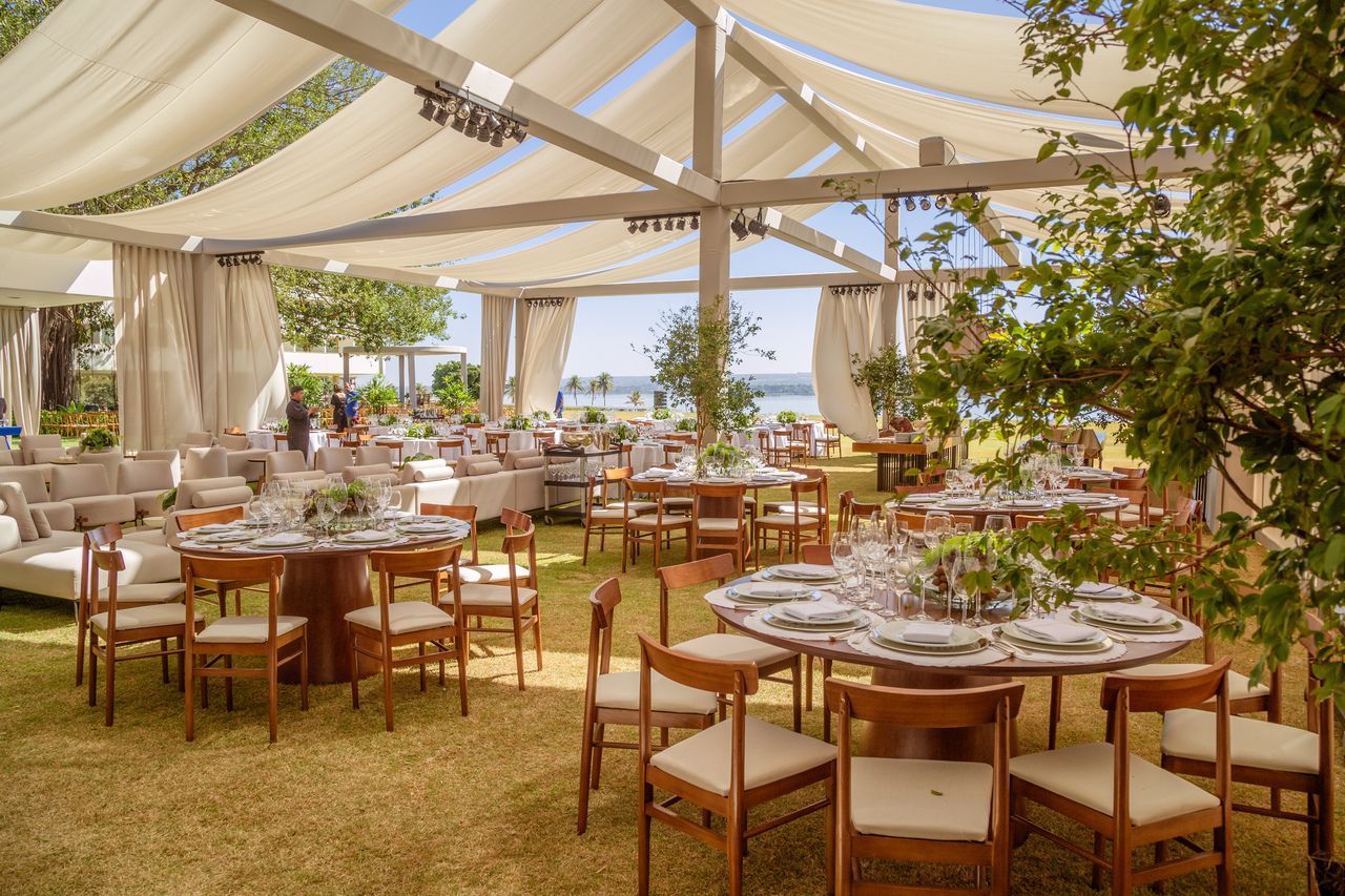 Recepção de casamento ao ar livre com mesas, cadeiras e uma tenda com vista para um corpo d'água.