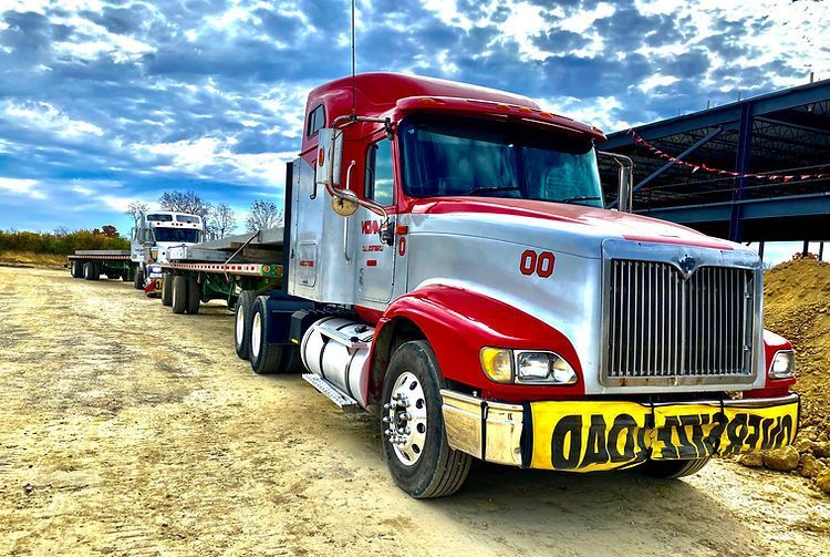 A red and silver semi truck is parked in a dirt lot