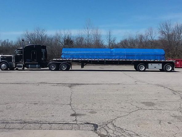 A semi truck with a blue tarp on the trailer is parked in a parking lot