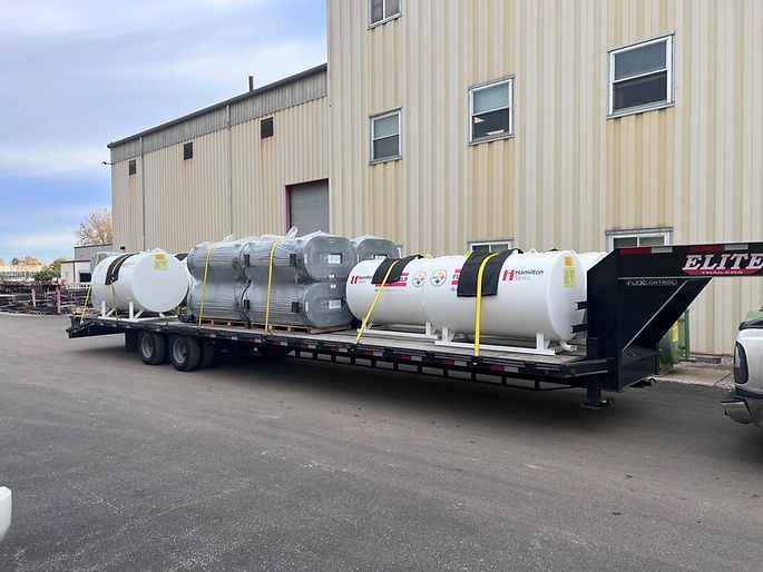 A trailer with a lot of tanks on it is parked in front of a building