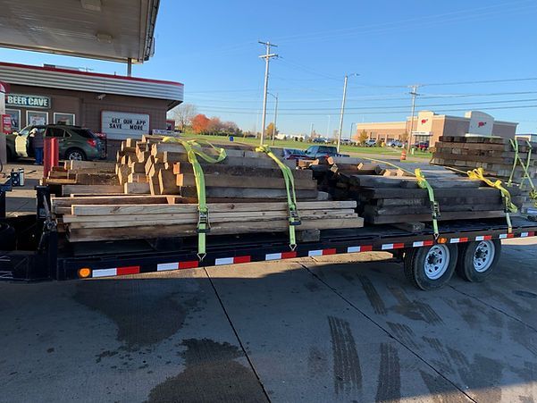 A trailer filled with wooden logs is parked in front of a gas station