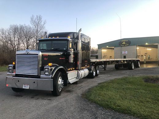 A semi truck with a flatbed trailer is parked in front of a building