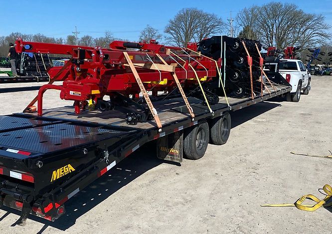 A trailer with a tractor on it is being towed by a truck