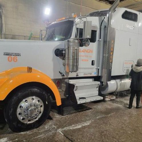 A white semi truck with orange fenders is parked in a garage