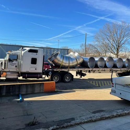A semi truck is carrying a bunch of pipes on a trailer